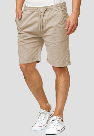 Beige bomullsshorts med resårmidja och dragsko, utrustade med sidofickor och en avslappnad passform, kombinerade med vita sneakers.