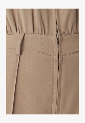 Beige-asu, jossa on kerrostettu yläosa, vetoketjukiinnitys takana ja sileä kangaspinta, joka on muotoillultaan jämäkkä.