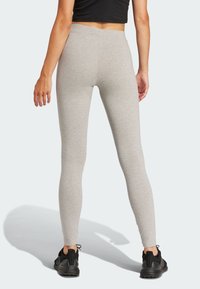 Szürke leggings, rugalmas anyagból készült, magas derékkal, testhezálló kialakítással, fekete sportcipővel párosítva.