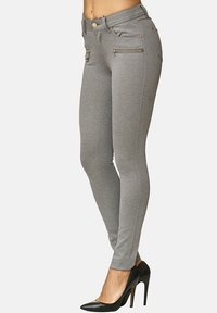 Leggings in denim grigio con una silhouette aderente, caratterizzati da tasche frontali con zip e dettagli in oro. Indossati con scarpe con tacco nere.