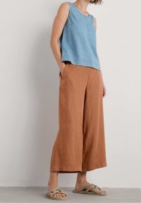 Light blue sleeveless denim top with a round neckline, paired with brown wide-leg trousers and braided sandals. Simple design, casual look.