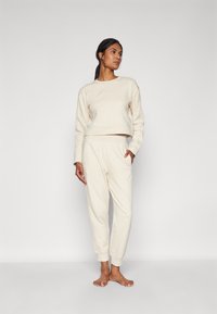 Felpa corta beige e pantaloni abbinati in tessuto morbido, con polsini elasticizzati, tasche laterali e dettagli del logo sottili.