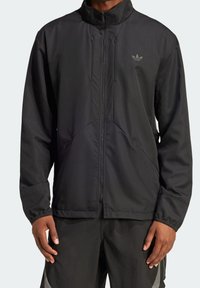 Black athletic jacket with a high collar, zippered front, and textured fabric. Features two side pockets and a small logo on the chest.