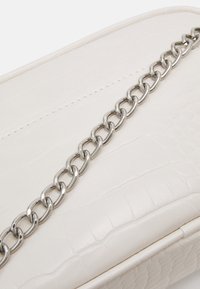 Bílá taška z umělé kůže s texturovaným krokodýlím vzorem a výrazným stříbrným řetízkem. Hladký povrch s prošívanými detaily.