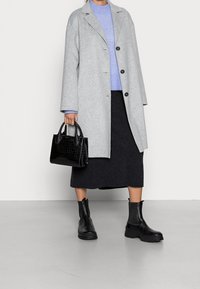 Szary wełniany płaszcz z czarnymi guzikami, zestawiony z jasnoniebieskim swetrem i ciemnografitową spódnicą midi. Czarna torebka w tłoczenie krokodyla i czarne botki za kostkę.