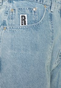 Jeans de mezclilla de color azul claro con una etiqueta de marca, herrajes plateados y costuras visibles a lo largo de los bolsillos y las costuras.