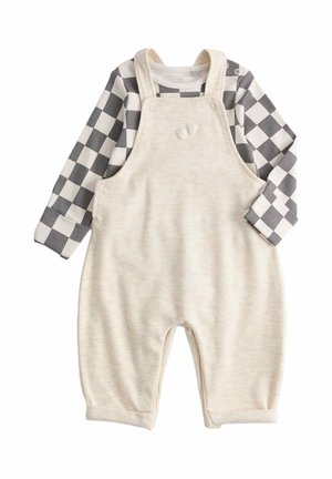 Crèmekleurig baby-overall met schouderbandjes en kleine voetjes borduursel, gecombineerd met een lange mouw zwart-wit geruit shirt.
