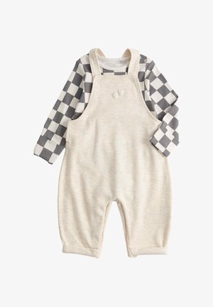 Tutina per neonati color crema con spalline e ricamo di piccoli piedini, abbinata a una camicia a maniche lunghe a quadretti bianco e nero.