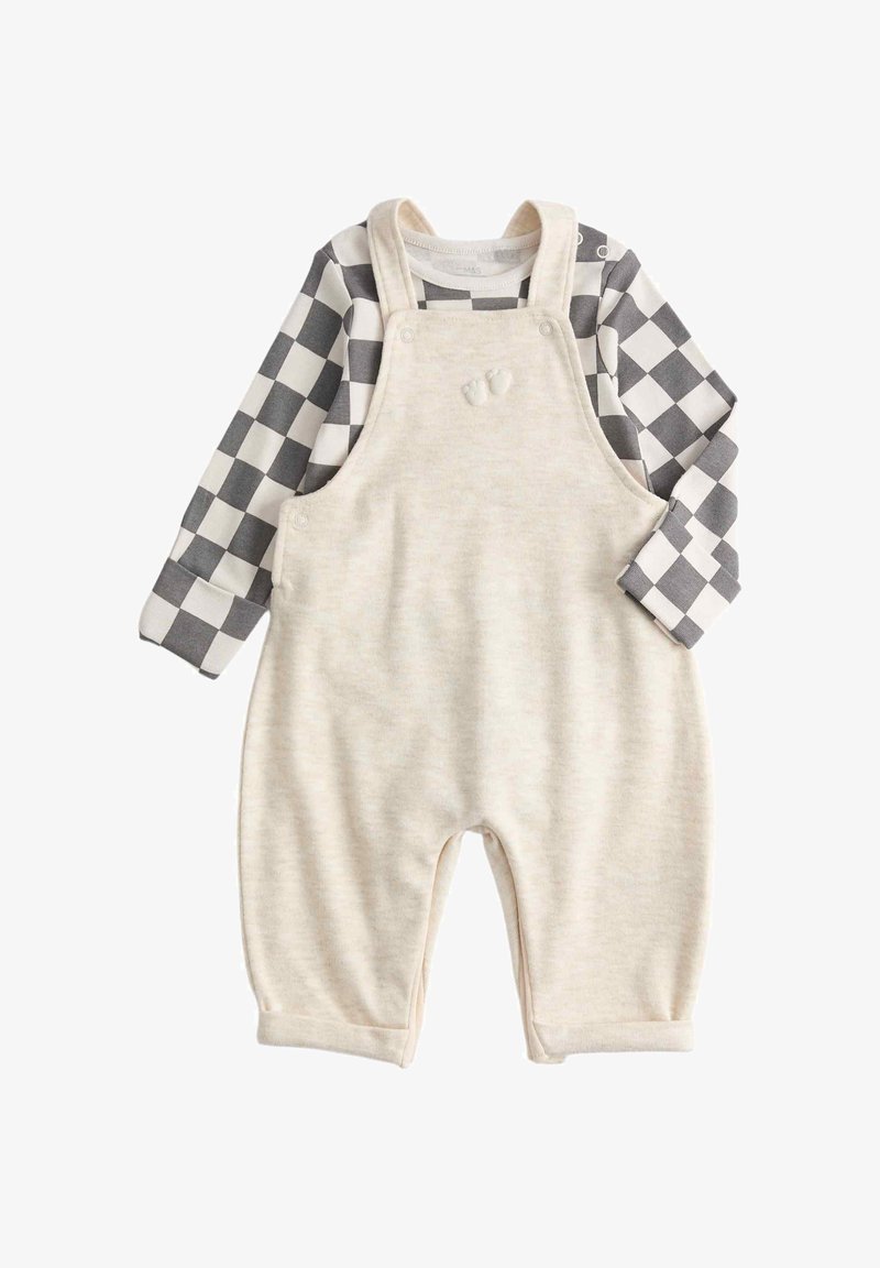 Kremowy kombinezon dla niemowląt z ramiączkami na ramionach i haftowanymi małymi stópkami, zestawiony z koszulą w czarno-białą kratę z długim rękawem.
