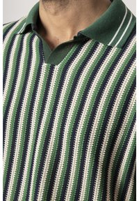 Pull en maille à rayures avec des rayures horizontales vertes, marine et crème, un col en V, et un col vert avec des rayures blanches en accent.