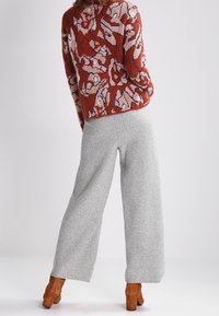 Strikket sweater i rødt med pinkt blomsterprint, kombineret med grå bukser med vide ben og brune støvler med hæl, set bagfra.