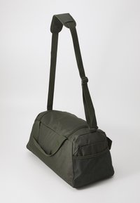 Groene stoffen sporttas met verstelbare schouderriem, handvat aan de bovenkant en een gaas-zijk pocket. Rechthoekige vorm met een gladde textuur.