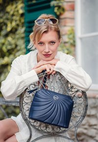 Námořnická kabelka se spirálovým prošíváním, stříbrným řetízkovým popruhem a logem. Hladká kožená textura a obdélníkový tvar.