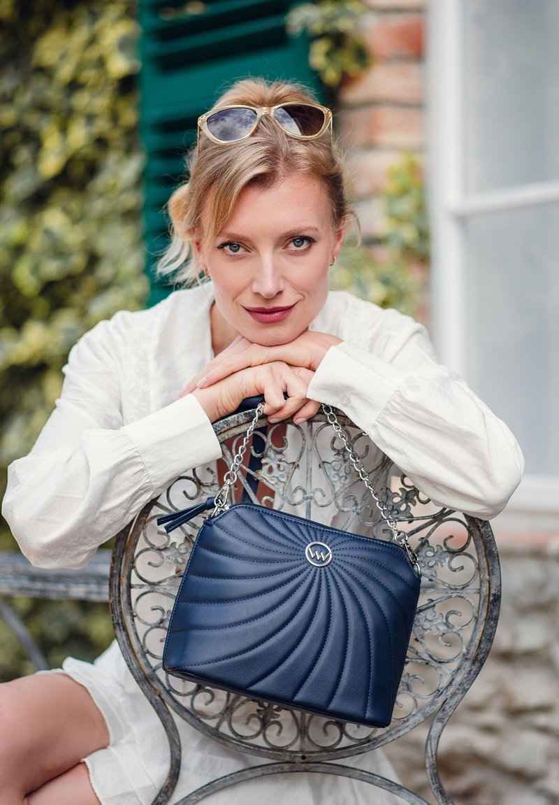 Námořnická kabelka se spirálovým prošíváním, stříbrným řetízkovým popruhem a logem. Hladká kožená textura a obdélníkový tvar.