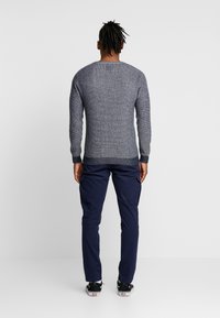 Grijze gebreide trui met geribbelde boorden en zoom, gecombineerd met marineblauwe cargobroek. De outfit heeft een losse pasvorm en een gestructureerde stof.