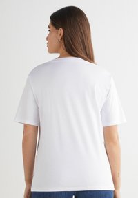 T-shirt bianca in cotone con colletto rotondo, maniche corte e vestibilità comoda. Presenta una superficie liscia e nessun motivo o design visibile.