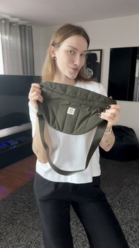 Olivgrüne Umhängetasche aus gestepptem Nylon. Sie hat eine abgerundete Form, ein Logo-Patch und einen verstellbaren Riemen.