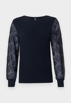 Tummansininen neulepusero, jossa on läpinäkyvät kukkakuvioiset pitkät hihat ja ribbaatut hihansuut, pyöreä kaula-aukko ja suora helma.