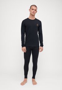 Svart långärmad topp och tighta leggings i stretchmaterial. Har en liten logotyp på bröstet och långa ärmar. Inga mönster eller detaljer.