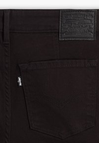 Jeans de mezclilla negra con un parche de cuero de la marca, bolsillo trasero con detalles de costura y etiqueta de Levi's en la costura lateral.