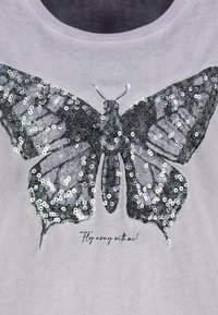 Graues Stoff-T-Shirt mit einem großen Schmetterlingsdesign aus silbernen Pailletten, darunter der Text "Flieg mit mir davon!"