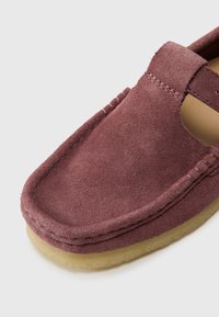 Burgundijas zamša slip-on kurpes ar noapaļotu purngalu, ar šūtu apdari un mīkstu bežīgu zoli. Iekļautas izgrieztas detaļas gaisa caurlaidībai.