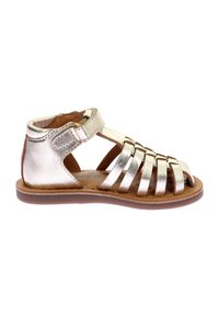 Sanda hecha de metal dorado con múltiples correas, cierre en el tobillo y una suela plana marrón. Diseñada para la transpirabilidad y la comodidad.