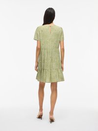 Abito verde con design a strati, maniche corte e dettaglio a chiave sul retro; presenta un motivo sottile e un tessuto leggero.