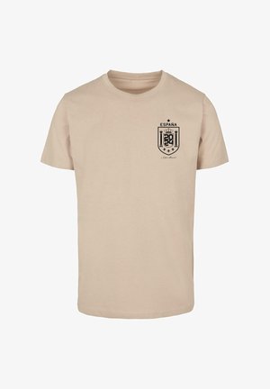 Šviesiai rudas medvilninis marškinėlis su juodu spauduoto šarvo logotipu, ant kairiojo krūtinės puikuojasi "ESPANA" ir "2024". Klasikinis apvalios iškirptės dizainas.