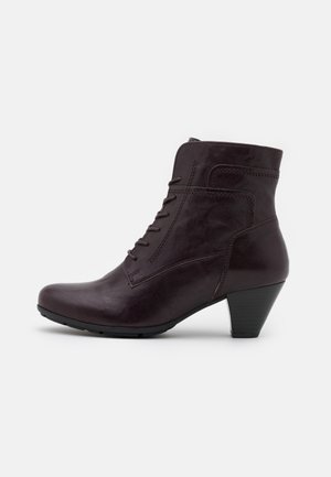 Ciemnobrązowy skórzany botek za kostkę z przodem na sznurowadła i niskim, warstwowym obcasem, pokazany z zewnętrznej strony na białym tle.