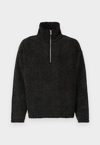 Pullover de forro polar negro con cuello alto y media cremallera. Tejido texturizado y suave con un corte holgado y mangas largas. Sin logotipos ni patrones visibles.