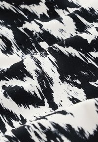 Tissu abstrait en noir et blanc avec des motifs de coups de pinceau irréguliers et une texture visible sur un matériau plié.