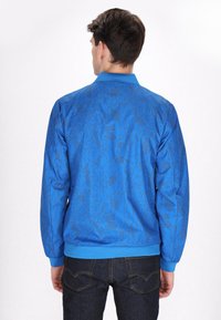 Giacca bomber blu con un motivo astratto nero, colletto e polsini a coste e una texture liscia. Progettata per una vestibilità casual.