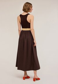 Robe longue marron avec un corsage en tricot texturé, une taille dorée et une jupe ample. Associée à des sandales à talons carrés rouges.