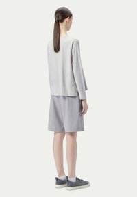 Ljusgrå långärmad topp med en avslappnad passform, tillsammans med grå skräddarsydda shorts och mörkgrå sneakers. Slät textur, minimalistisk design.