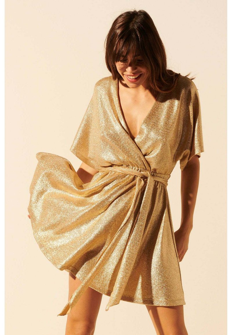 Robe portefeuille dorée, avec un décolleté en V profond et des manches courtes. Fabriquée dans un matériau scintillant ; nouée à la taille avec une ceinture assortie.