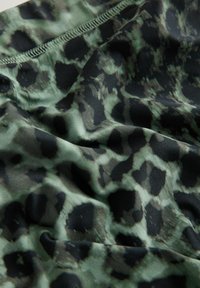 Tekstil med et grønt og sort leopardprintmønster. Glat tekstur, blandet stof, med diskret glans og syede kanter.