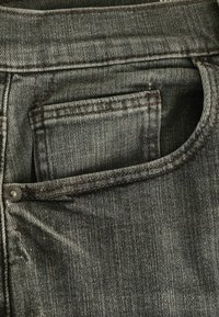 Gros plan sur la poche d'un jean en denim gris montrant les coutures, le rivet et la poche à monnaie à l'intérieur de la poche principale.