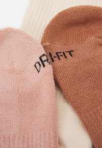 Tre paia di calze: rosa chiaro, beige con righe verticali e marrone ruggine con "DRI-FIT" in nero, che mostrano una superficie a maglia liscia.