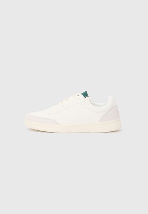 Sneaker blanc avec une tige en cuir lisse, des accents en daim gris sur le bout et le talon, un onglet de languette vert, et une semelle en caoutchouc texturée.