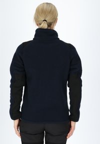 Navy fleece jacket with high collar, black sleeve accents, textured fabric, and elastic cuffs, designed for comfort and warmth.
