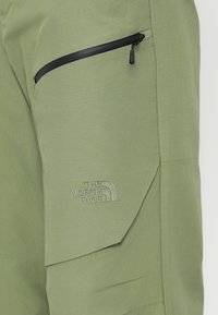 Pantaloni tehnici de culoare verde deschis, cu o textură uniformă, buzunar cu fermoar și logo brodat "The North Face" în culoarea firului asortată.
