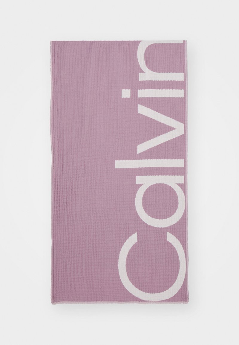 Coperta di cotone viola chiaro con una grande scritta bianca "Calvin", caratterizzata da una superficie testurizzata e bordi orlati.