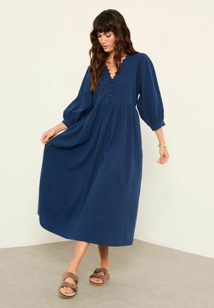 Marineblaues, gewebtes Maxikleid mit Puffärmeln, einem V-Ausschnitt und Knopfdetails. Der Stoff hat ein dezentes, strukturiertes Muster.