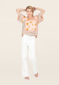 Blusa a fiori rosa con maniche ampie, abbinata a jeans bianchi a vita alta e sandali rosa con cinturini.
