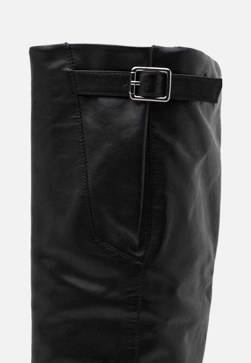 Botte noire en cuir montante, présentant une texture lisse, une forme arrondie et un accent en boucle argentée sur le côté.