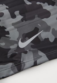 Sort og grå camouflagemønsteret stof med glat tekstur. Har et reflekterende sølv Nike-logo i nederste venstre hjørne.