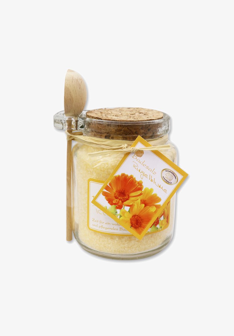 Ein Glasbehälter mit gelben Badezusatz, Korkdeckel, Holzlöffel und einem gelben Etikett mit orangenen Blumen. Umwickelt mit natürlichem Twine.