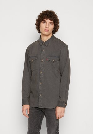 Chemise en denim gris à manches longues, avec un devant à boutons, deux poches poitrine et un logo de marque subtil. Présente un col classique et des boutons foncés.