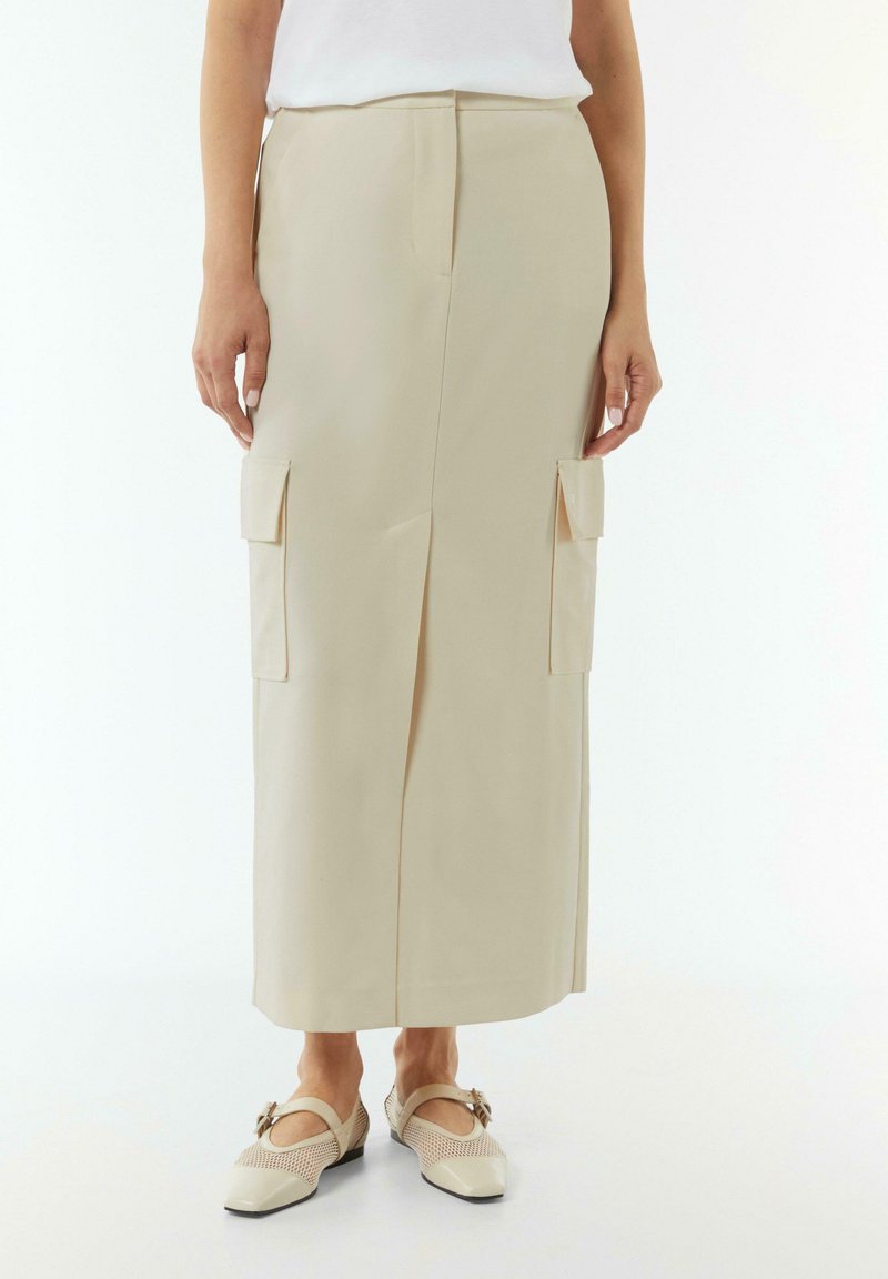 Beige cargo skirt with front slit, featuring two patch pockets on the sides. Smooth, textured fabric with a straight cut design.